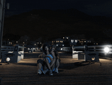 a man and a woman are sitting on a wooden pier at night