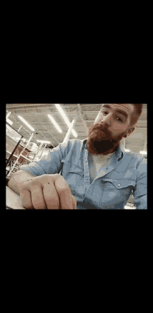 a man with a beard and a tattoo on his arm is sitting at a counter in a store .