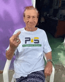 an elderly woman is sitting in a chair wearing a white t-shirt and giving the middle finger .