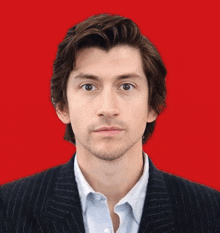 a man with a beard wearing a suit and a white shirt against a red background