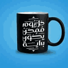 a black mug with arabic writing on it is sitting on a blue surface .