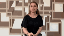 a woman in a black shirt is sitting in front of a geometric pattern