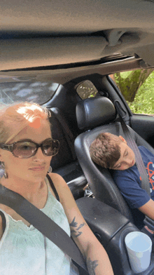 a woman wearing sunglasses is sitting in a car with a boy sleeping in the back seat