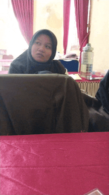 a woman in a hijab sits at a table with a water bottle in front of her