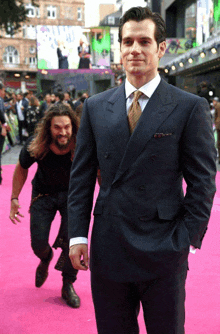 a man in a suit is standing on a pink carpet