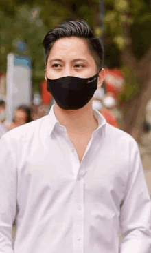 a man wearing a white shirt and a black mask is walking down a street .