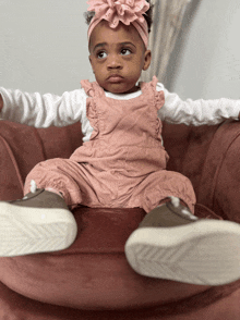 a little girl wearing overalls and a headband is sitting on a couch