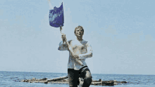 a man is holding a blue flag on a stick in the ocean .