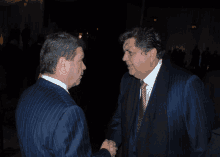 two men in suits and ties are shaking hands in a dark room