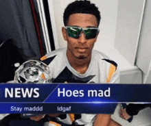 a man wearing sunglasses is holding a trophy in front of a news sign that says hoes mad