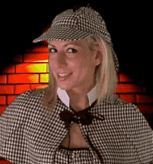 a woman in a cape and hat is smiling in front of a brick wall .