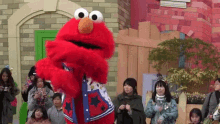 elmo from sesame street is standing in front of a group of people .