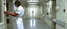 a man in a white uniform is washing his hands in a hospital hallway with an exit sign above him