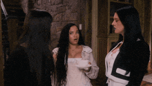 three women are standing in a room and one of them is holding a cup