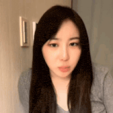 a woman with long dark hair is wearing a gray sweater and looking at the camera .