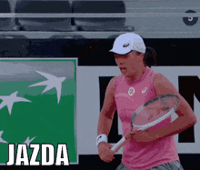 a woman in a pink tank top is holding a tennis racquet in front of a sign that says " jazda "