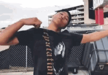 a man in a black shirt is standing with his arms outstretched in front of a chain link fence .