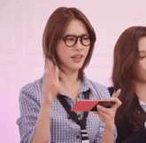 a woman wearing glasses and a plaid shirt is holding a phone