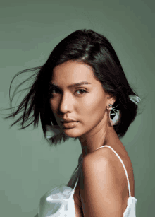 a woman wearing a white top and feather earrings looks at the camera