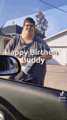 a man is standing in front of a car and holding a piece of paper that says happy birthday buddy