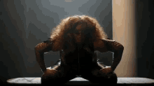 a woman with curly hair is sitting on a table with her hands on her knees .