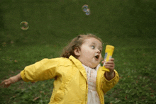 a little girl wearing a yellow jacket is blowing soap bubbles