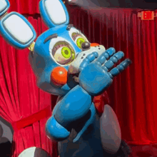 bonnie the bunny from five nights at freddy 's is standing on a stage in front of a red curtain .