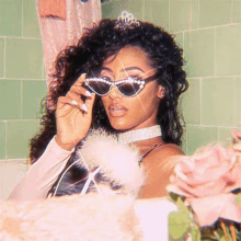 a woman wearing sunglasses and a tiara is standing in front of a mirror in a bathroom .