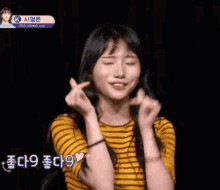 a girl in a yellow striped shirt making a heart with her hands