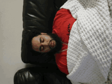 a man in a red shirt is sleeping on a couch with a white blanket over him