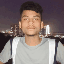 a young man with a backpack stands in front of a city skyline at night