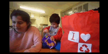 a woman and a child are sitting at a table with a bag that says i love recycling on it .