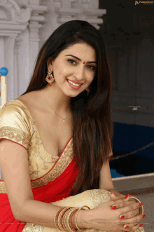 a woman wearing a red saree and gold blouse is smiling for the camera