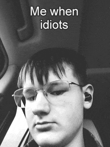 a young man wearing glasses and ear buds is sitting in a car with a caption that says me when idiots