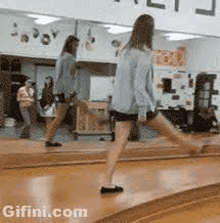 a woman is walking on a wooden floor in front of a mirror in a dance studio .