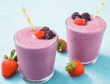 two smoothies with strawberries and blackberries on top on a blue surface