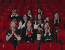 a group of women are sitting in red seats at a movie theater .