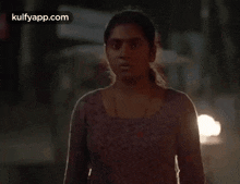 a woman in a purple shirt is walking down a street at night with a car in the background .