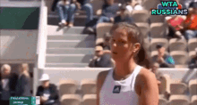 a woman in a white tank top stands in front of a crowd at a tennis match with the words wta russians on the bottom