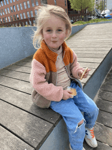 a little girl sitting on a wooden ledge eating a cookie