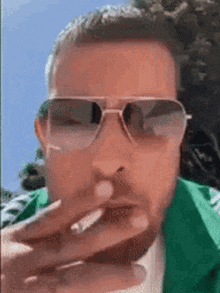 a man wearing sunglasses and a green jacket smoking a cigarette