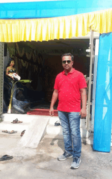 a man in a red shirt and blue jeans stands in front of a building