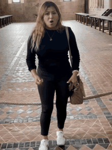 a woman wearing a black sweater and white sneakers is standing in a hallway