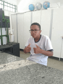 a boy wearing glasses giving a thumbs up in a room