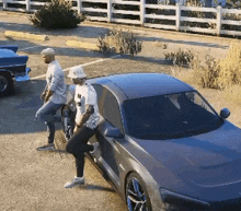 two men are standing next to a gray sports car