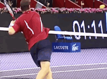 a man in a red shirt is swinging a tennis racket on a tennis court in front of a lacoste sign