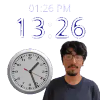 a man wearing glasses stands next to a clock that says 12:26 pm