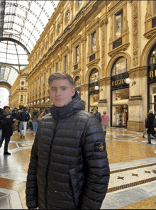 a man in a black jacket stands in front of a building with the word rizzo on it