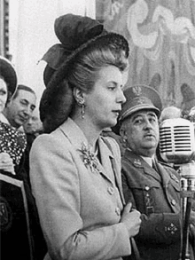 a black and white photo of a woman in a hat standing in front of a microphone .