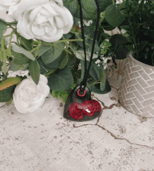 a necklace with a heart shaped pendant with red flowers on it